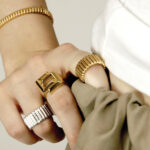 De gauche à droite, bagues : à l'annulaire : bague 82 en or blanc 18 carats et diamants COPIN, au majeur : bague C en or jaune COPIN, bague et bracelet 82 en or jaune 18 carats COPIN. Julia porte un débardeur PETIT BATEAU, pantalon XXL HIGHLIGHT STUDIO.